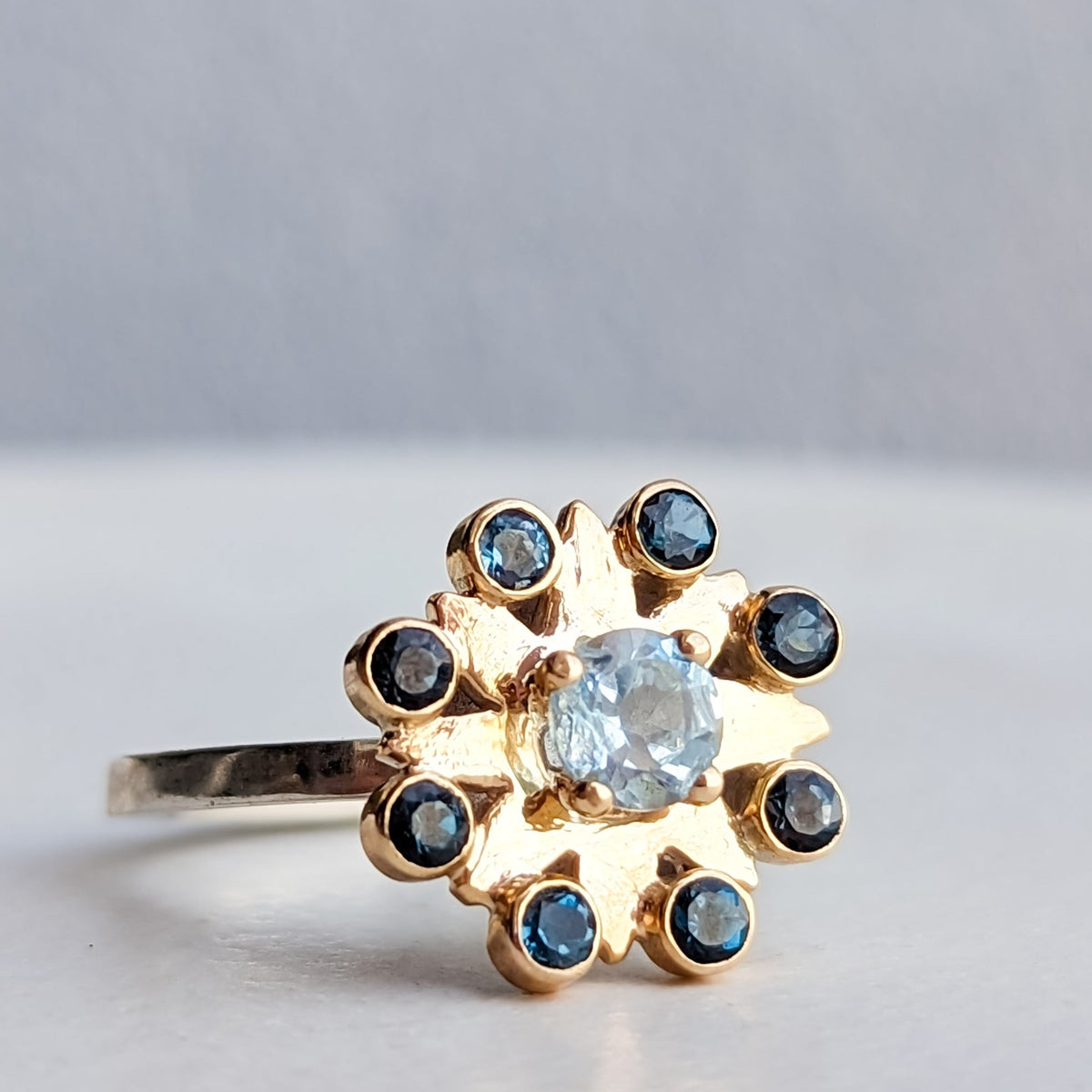 Gold and silver flower ring with a sky blue topaz centre and darker London blue topaz stones.