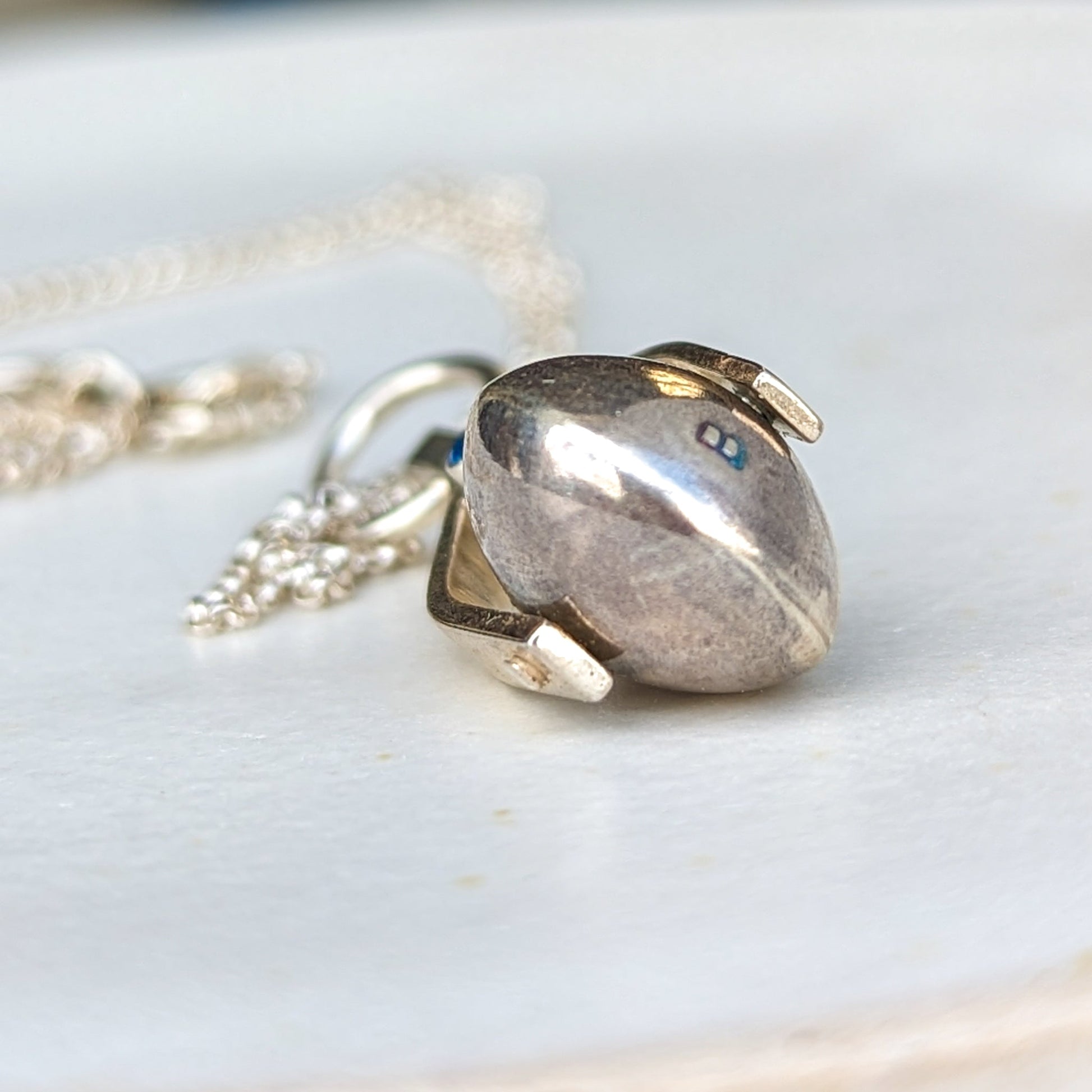 Detailed shot of the spinning moon necklace in sterling silver with a blue gemstone, showcasing its unique design as seen in 'Playing Nice.' by Booblinka Jewellery