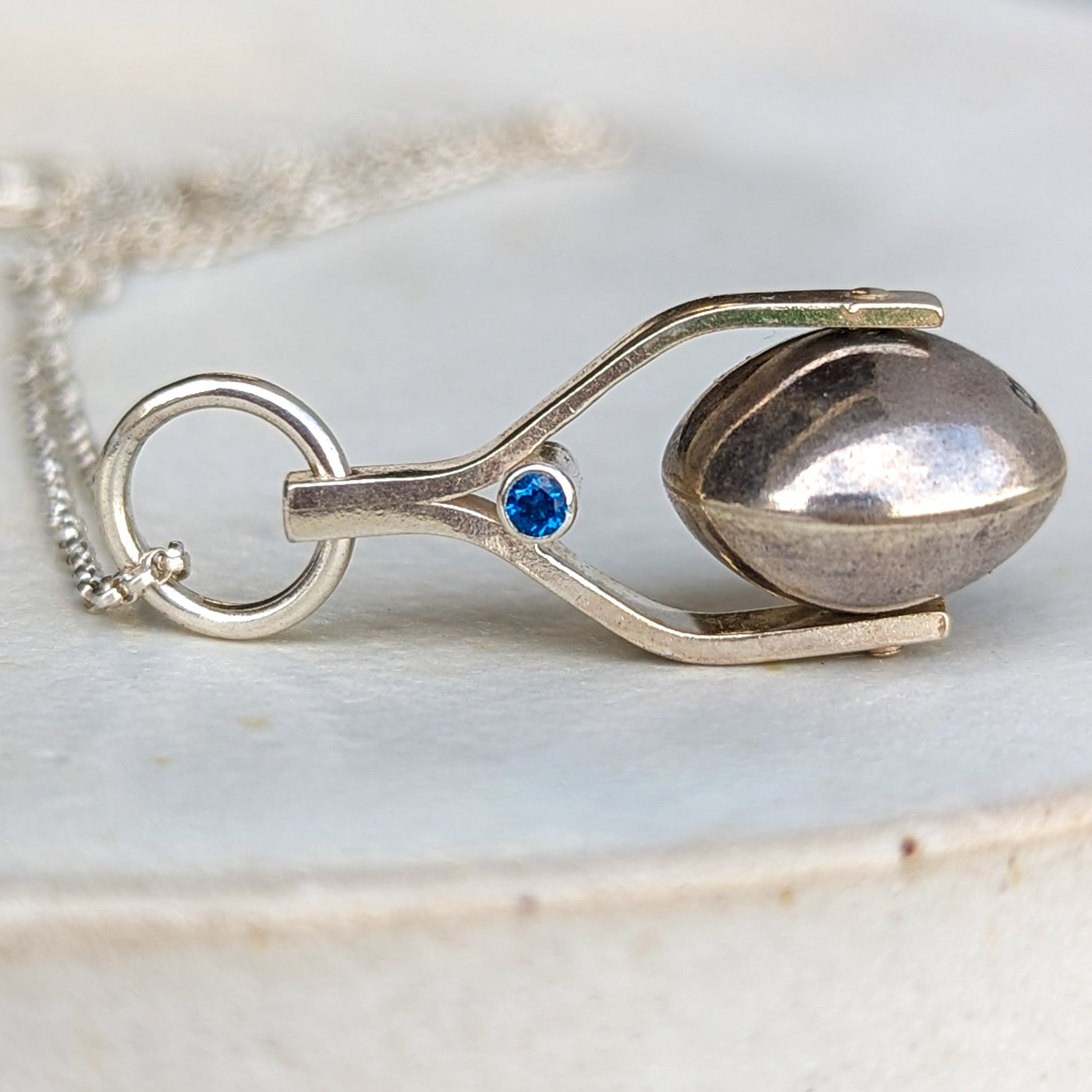 Detailed shot of the spinning moon necklace in sterling silver with a blue gemstone, showcasing its unique design as seen in 'Playing Nice' by Booblinka Jewellery 